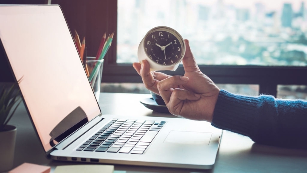 Businessman holding clock on computer laptop in home office