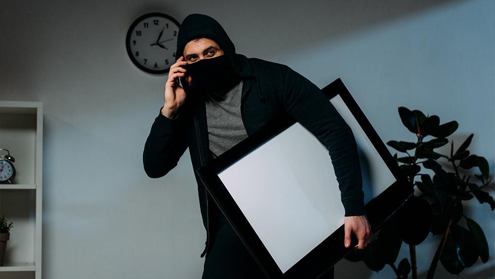 Burglar in mask talking on smartphone carrying tableau