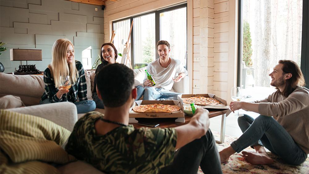 Group of people eating pizza and relaxing in a house