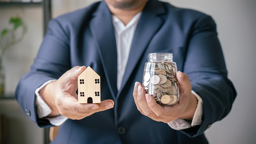 Saving money by buying property concept, a man holding house model coins in a jar