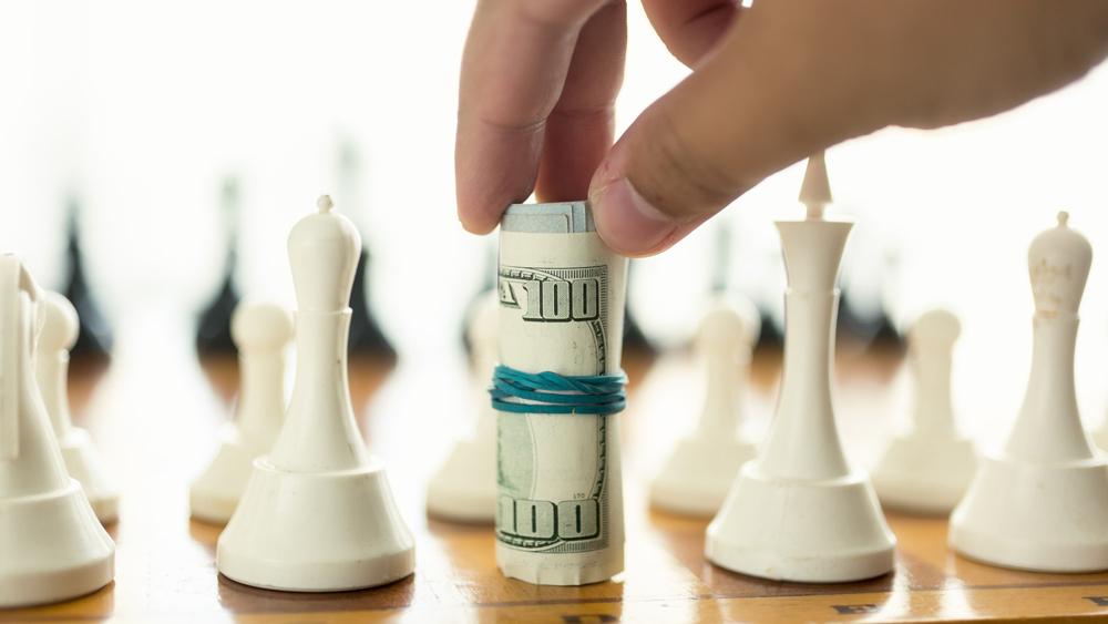 Closeup of man making move in chess with twisted money